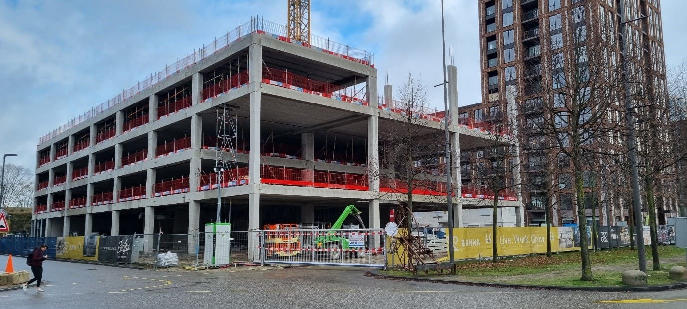 Het betonnen casco van de kantoorlagen in aanbouw, met rode randbeveiliging.