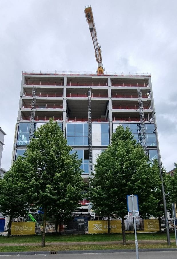 Gebouw DONNA in aanbouw met bouwkraan, gezien tussen twee bomen.
