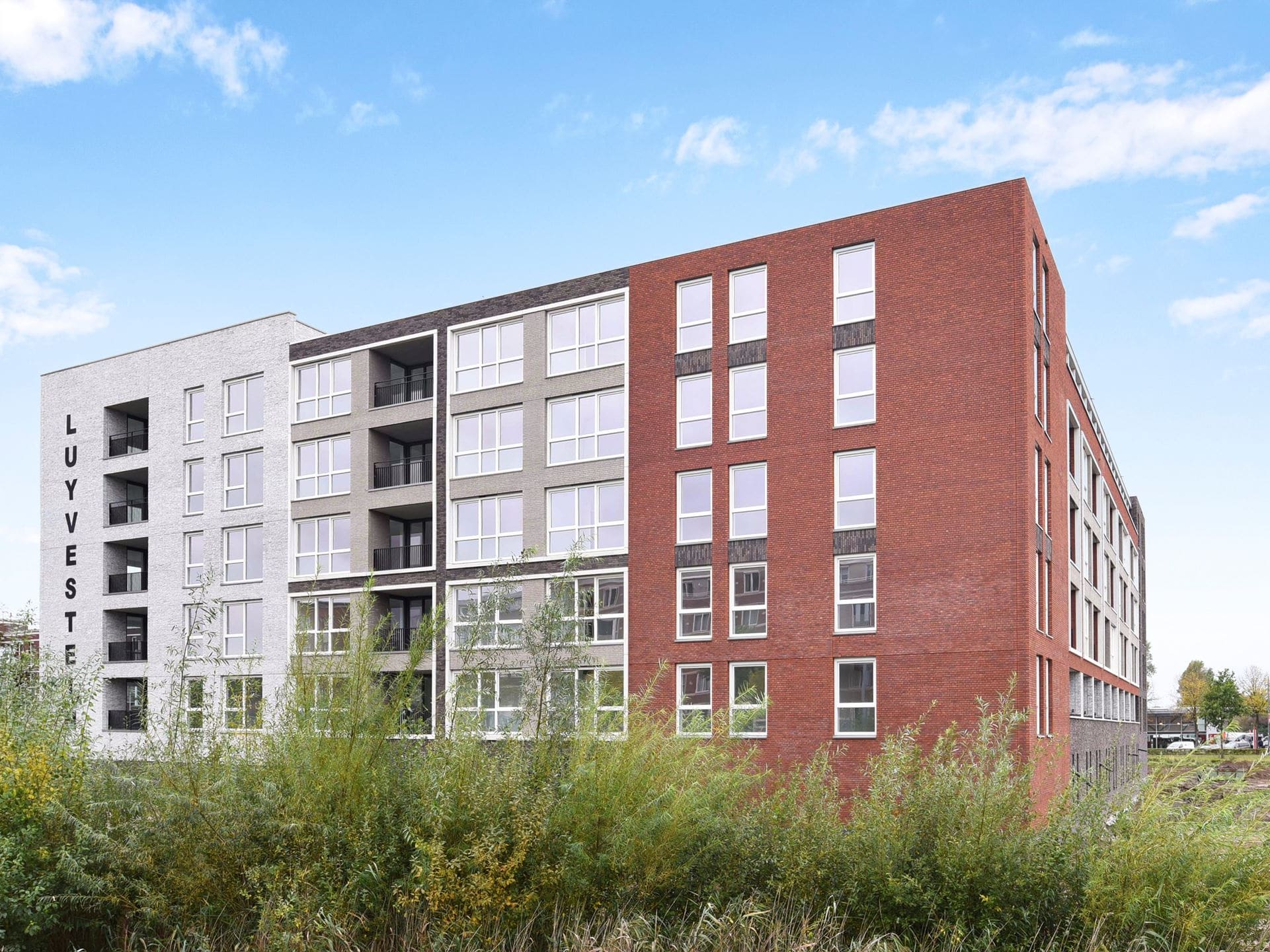 Het appartementengebouw Waterburcht W3 met gevels van rode, grijze en lichte baksteen, gezien over het riet.