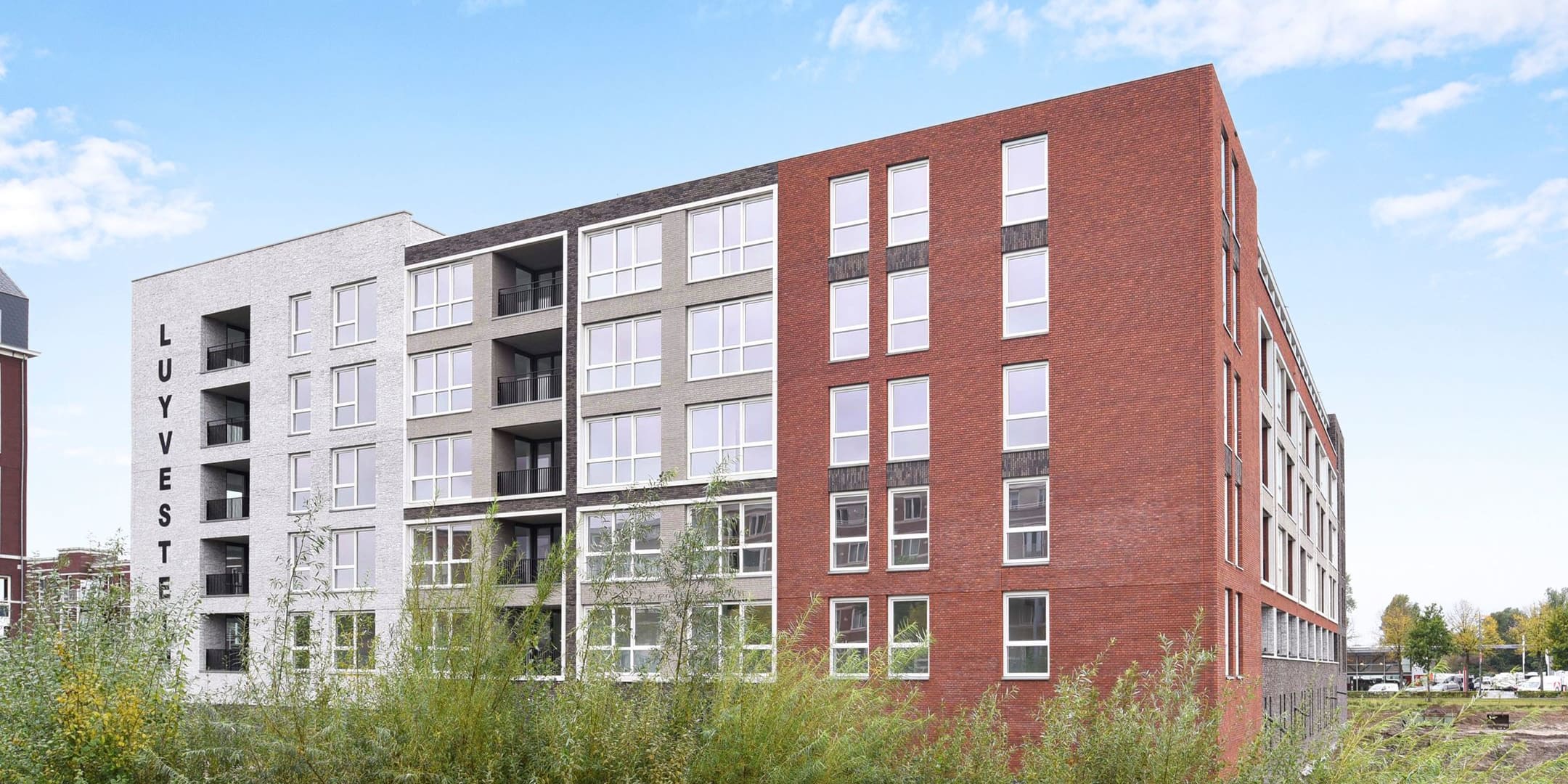 Het appartementengebouw Waterburcht W3 met gevels van rode, grijze en lichte baksteen, gezien over het riet.
