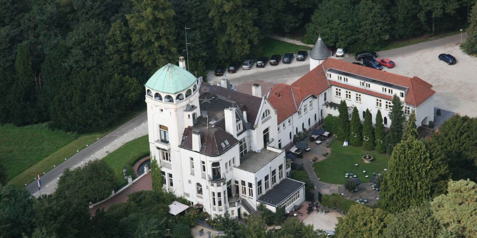 Luchtfoto van Jachtslot De Mookerheide, een wit landhuis met torens en rode daken tussen de bomen.