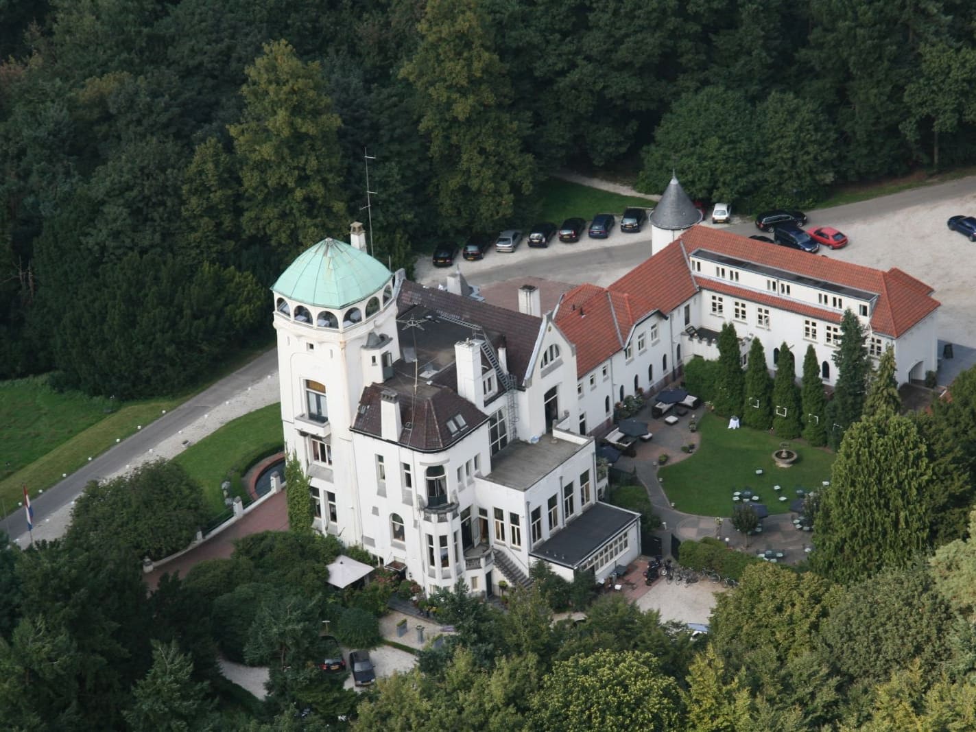 Luchtfoto van Jachtslot De Mookerheide, een wit landhuis met torens en rode daken tussen de bomen.