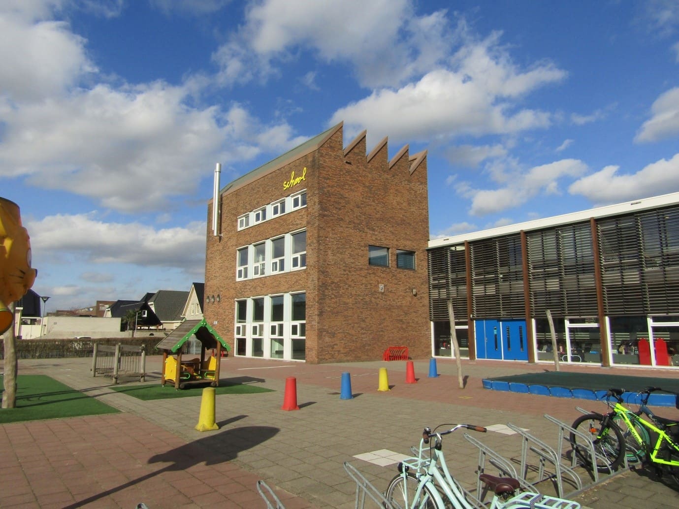 Een bakstenen schoolgebouw met een getrapte gevel en een schoolplein met fietsen.