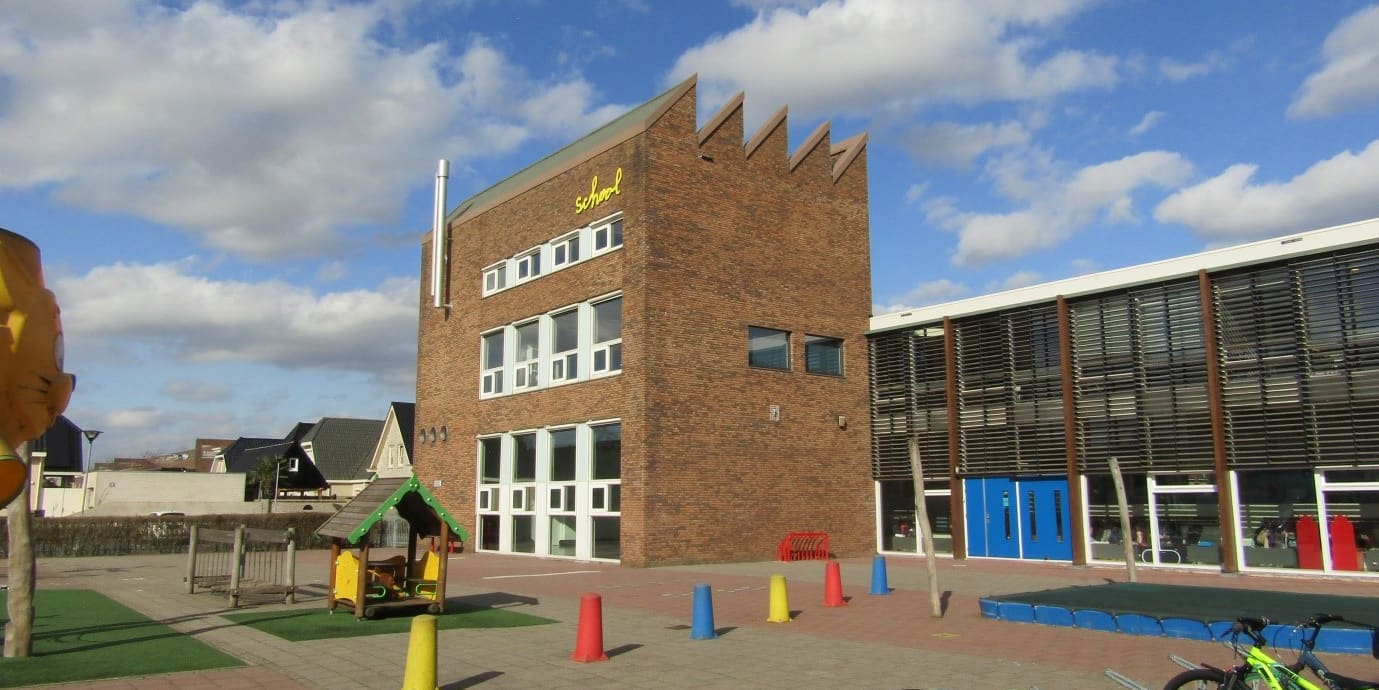 Een bakstenen schoolgebouw met een getrapte gevel en een schoolplein met fietsen.